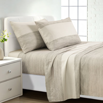 A neatly made bed with beige and off-white striped bedding, including two pillows and a matching duvet cover, shown in a bright bedroom setting with a white nightstand and window. #color_quiet-horizon-taupe