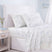 White bedding set with a delicate blue and green floral print, styled on a bed with a white upholstered headboard, a light wood nightstand, and a soft window curtain. #color_soft-bloom-blue