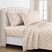 A neatly made bed with a cream sheet set featuring a delicate tan leaf pattern, styled with matching pillowcases and a tufted cream headboard in a bright bedroom. #color_willow-grove-rust