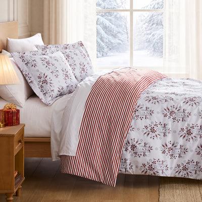 Merry Manor duvet cover set styled on a Christmas bed with white floral print, red striped reverse, matching shams, and festive decor.